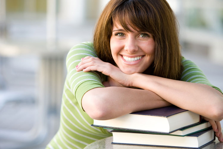 Woman smiling leaning on a stack of books