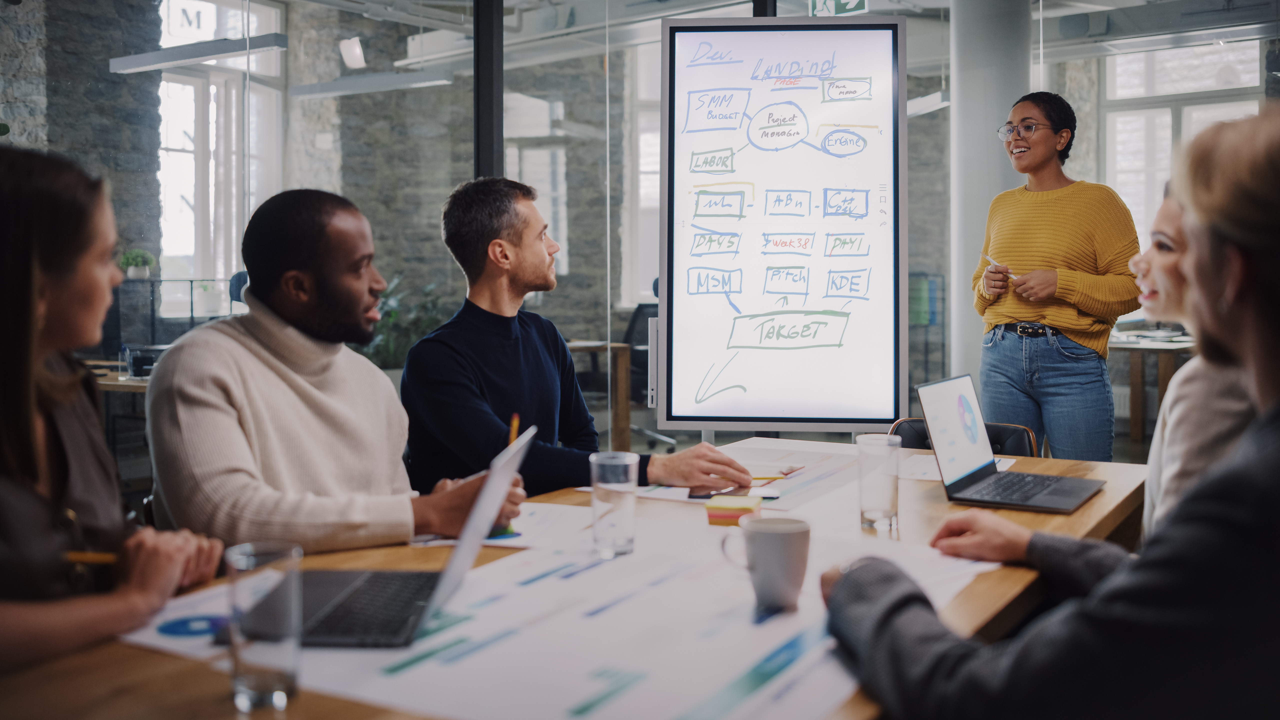 project meeting with several people. Woman standing in front of whiteboard smiling.